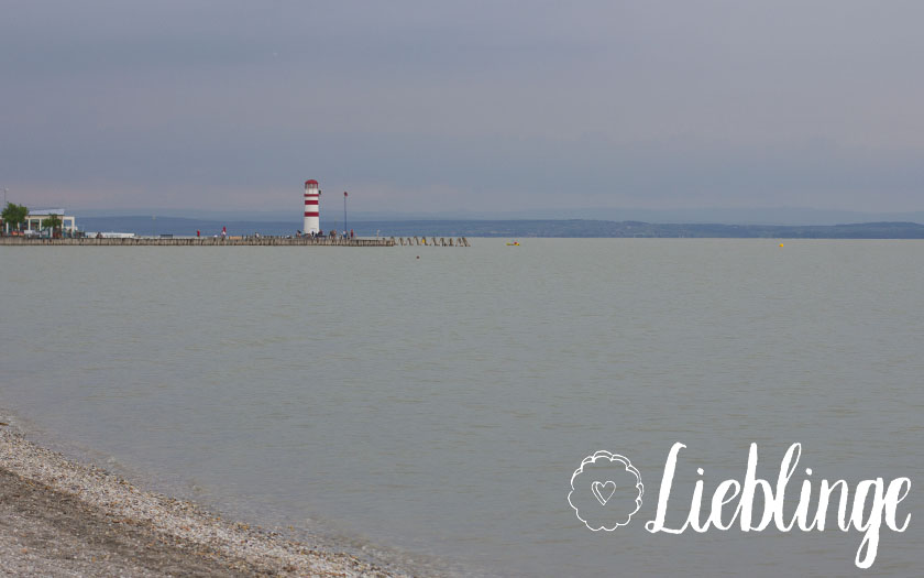 ausblick auf den grauen neusiedlersee, leuchtturm im hintergrund, lieblinge-schriftzug und lieblingsplätzchen-logo im vordergrund