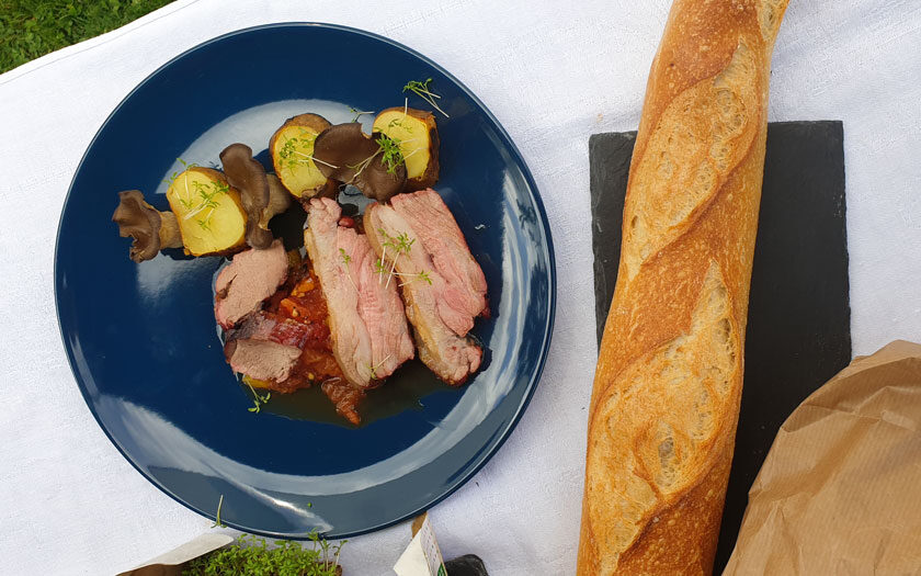 Ein Teller mit Fleisch, Letscho, Erdäpfeln und Pilzen, daneben Baguette